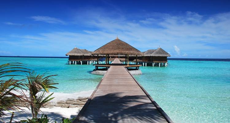 Overwater bungalows with straw roofs on a crystal clear turquoise sea.