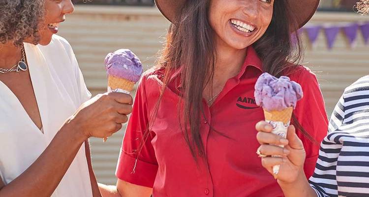 Group of friends laughing and holding purple ice-cream cones during a sunny outing.