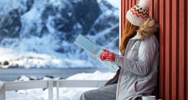 Woman reading a map on a snowy porch with a mountain view.