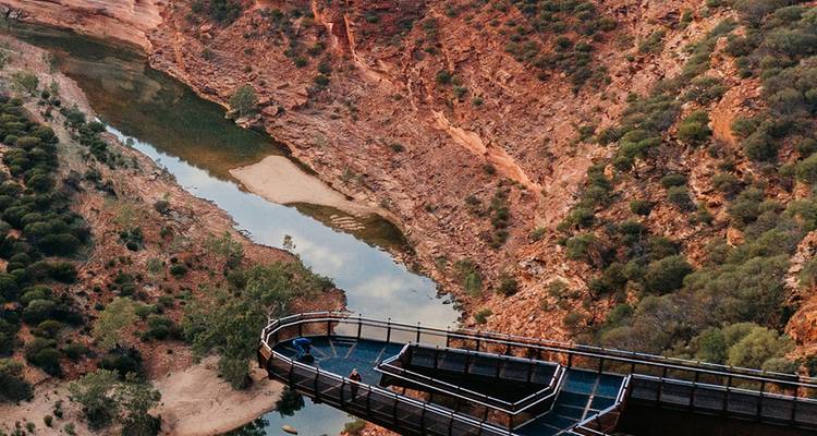 Elevated walkway overlooking a river gorge with red rock formations.