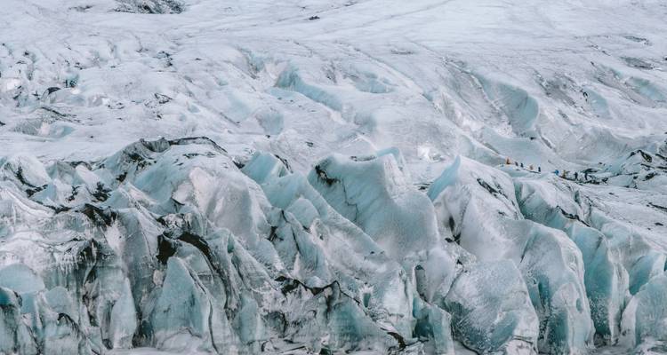 Paisaje glaciar helado con personas haciendo senderismo sobre las formaciones de hielo.