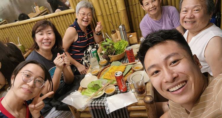 Un groupe de personnes souriantes à une table avec des plats vietnamiens traditionnels dans un cadre chaleureux.