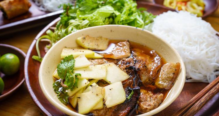 Un bol de Bun Cha avec des herbes, des nouilles et de la viande dans un cadre vibrant.