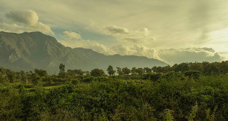 Lush landscape with mountains and vegetation under a cloudy sky.