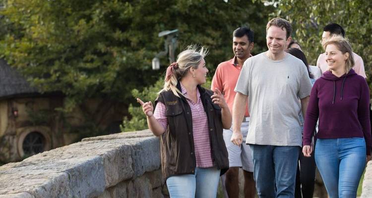 Guide discutant avec les visiteurs en marchant sur un pont de pierre dans un village de plateau de cinéma verdoyant.