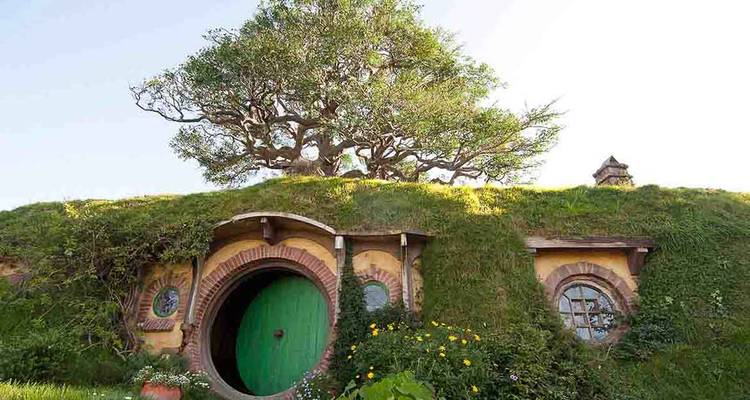 Porte ronde verte emblématique construite dans une colline herbeuse surmontée d'un vieux chêne.
