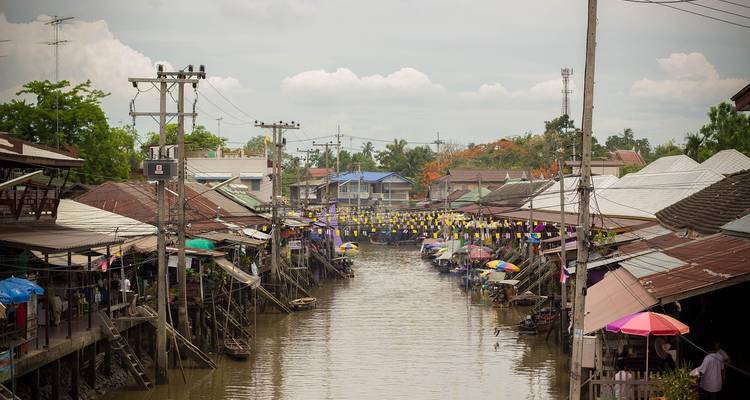 Marché de canal animé avec des parasols colorés et des maisons sur pilotis.