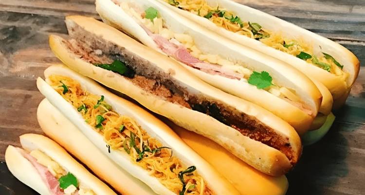Plusieurs sandwichs bánh mì disposés sur une planche en bois.