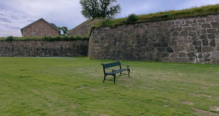 Mur de pierre et zone herbeuse avec un banc, possiblement un cadre de parc.