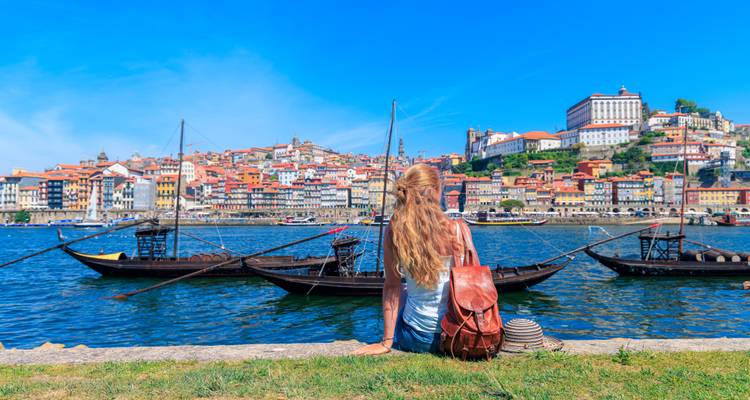 Woman sitting by the river looking at city buildings and boats.