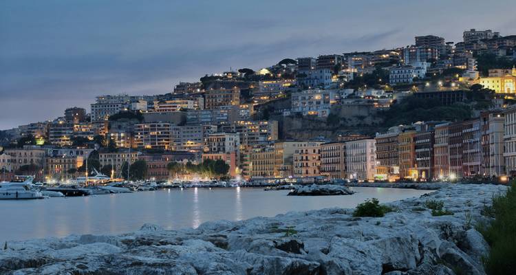 Evening view of Naples coastline with buildings lit up.