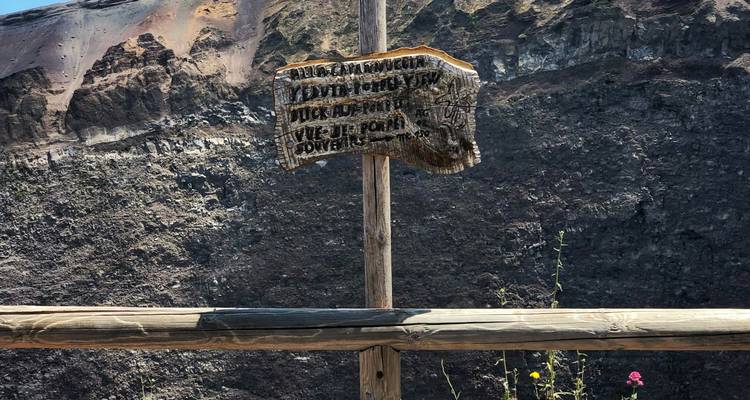 Wooden sign on mountain with volcanic crater in background.
