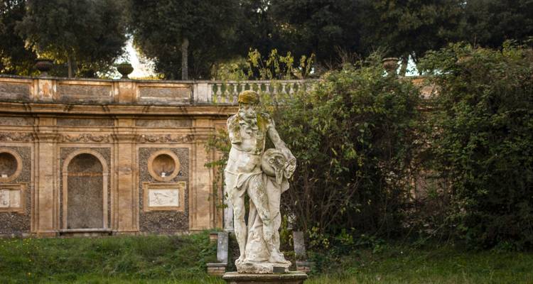 Statue in a lush garden surrounded by historic stone walls.