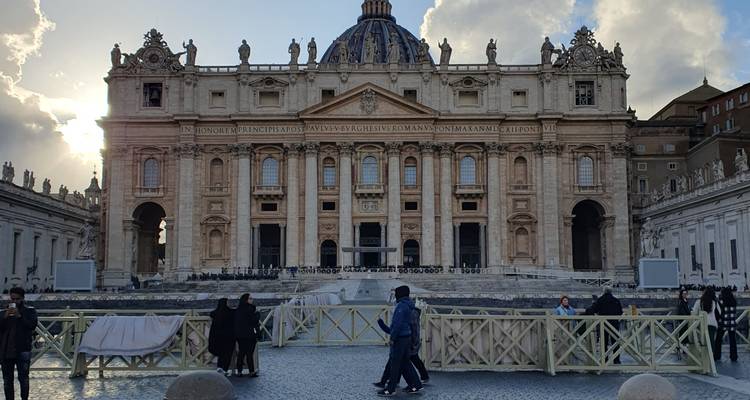 St. Peter's Basilica with people walking and clouds in the sky.