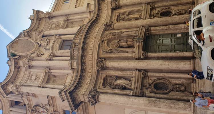 Facade of a historic building with sculptures and a vehicle in front.
