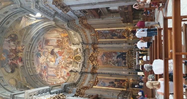 Interior of a grand church with frescoes and people inside.