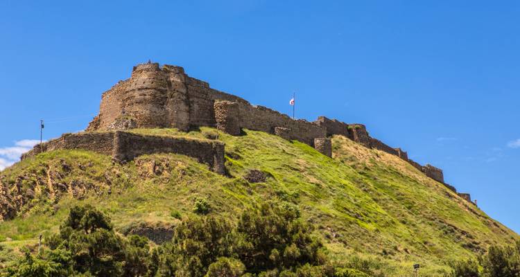 Ruines d'une ancienne forteresse sur une colline herbeuse sous un ciel bleu.