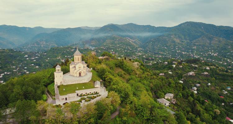 Église sur une colline entourée de verdure luxuriante et de montagnes lointaines.