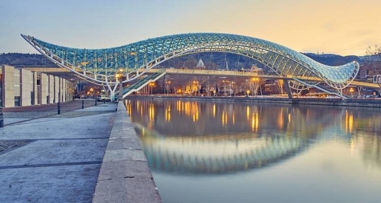 Pont moderne avec un design ondulé au-dessus d'une rivière au crépuscule.