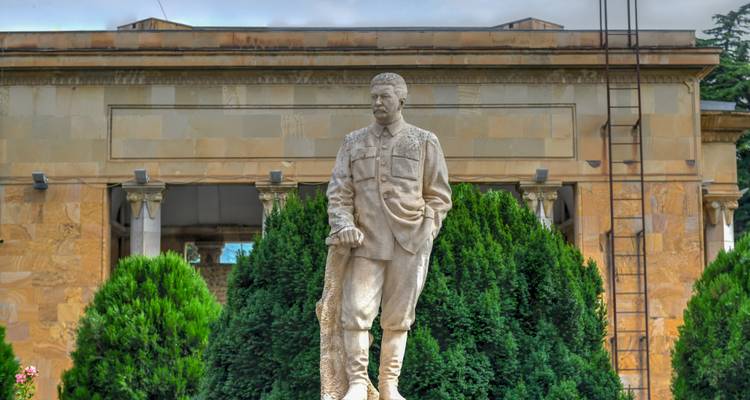 Statue eines Mannes vor einem Gebäude mit Bäumen.