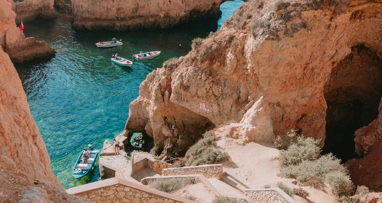 Small boats and people near turquoise waters and rocky cliffs.