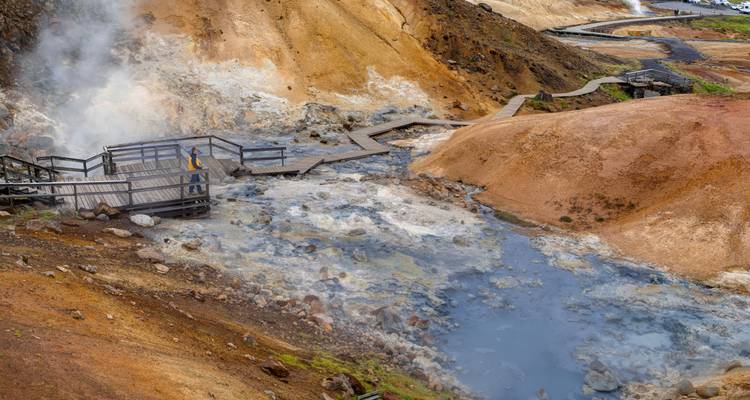 Zone géothermale fumante avec terre colorée et passerelle.
