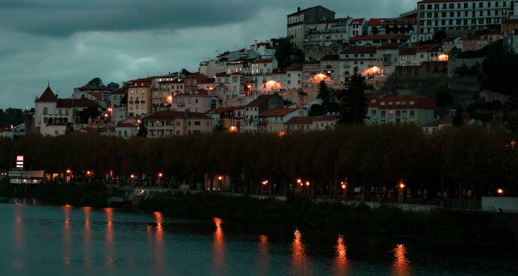 Stadsgebouwen langs een rivier in de schemering.