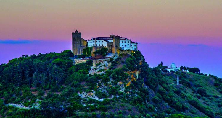 Castle on a hill under a colorful sunset sky.