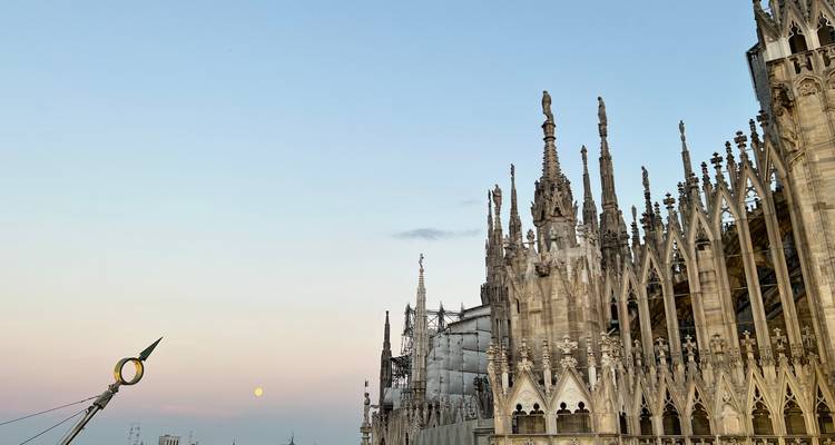 Torens van de Duomo di Milano met een pastelkleurige lucht op de achtergrond, met een gouden standbeeld.