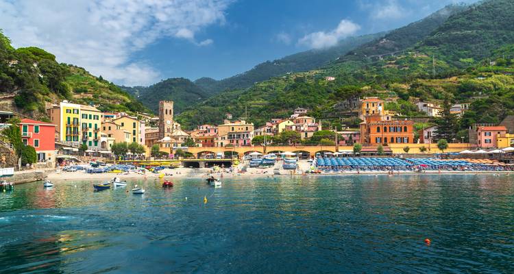 Kleurrijk kustdorpje met heuvels op de achtergrond en een heldere blauwe zee.