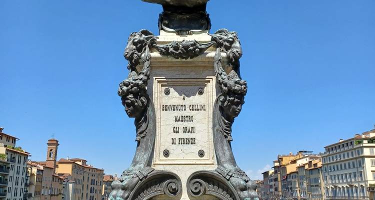 Sierlijke sculptuur met decoratieve elementen en stadsgebouwen op de achtergrond.