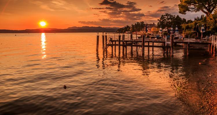 Prachtige zonsondergang boven een meer met een houten steiger, die warme tinten op het water weerkaatst.