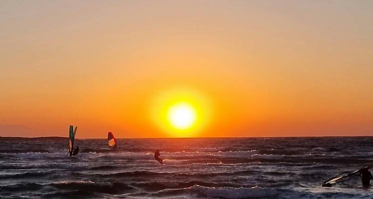 Atardecer sobre el mar con windsurfistas.