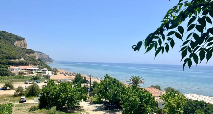 Blick auf Strand und Meer mit Bäumen im Vordergrund.