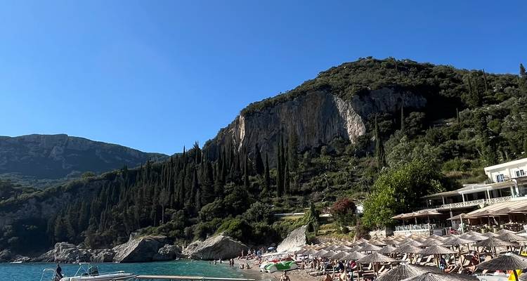 Strand mit vielen Liegestühlen und üppigem Hügel.