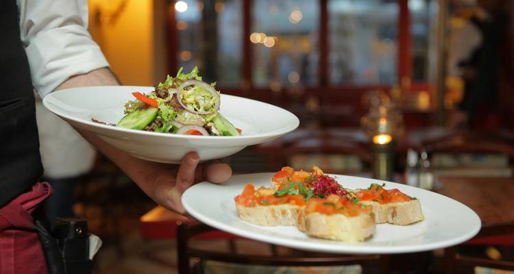 Hand serving plates of food in a restaurant.