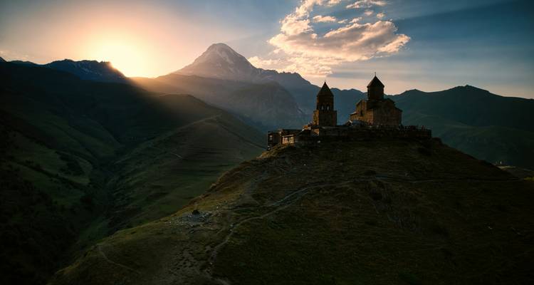 Église silhouettée sur un paysage montagneux au coucher du soleil.