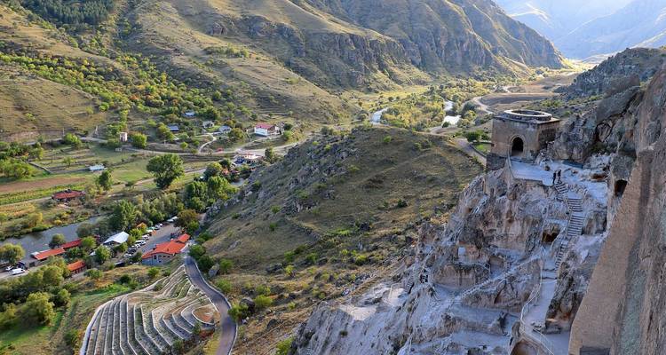 Vue d'une vallée et d'un village depuis une colline rocheuse avec des ruines antiques.