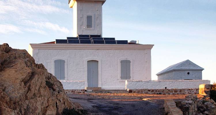 Faro blanco en una costa rocosa durante la puesta de sol