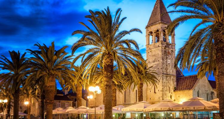 Night view of Trogir with palm trees and church tower.