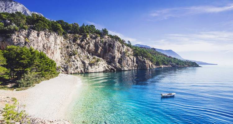 Peaceful beach with clear water and rocky cliffs.