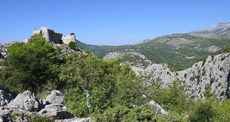 Historic fortress on a hilltop with mountainous landscape in the background.