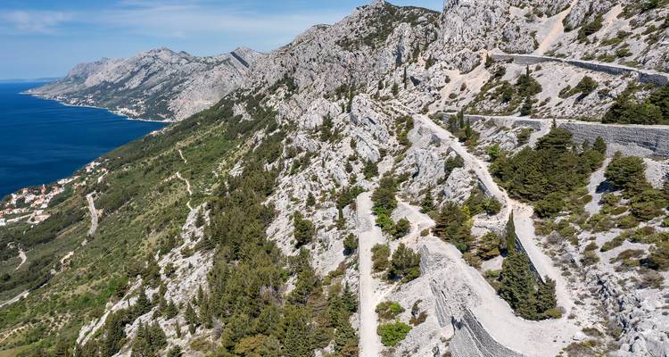 Winding mountain road along a rocky coastline with the sea visible.