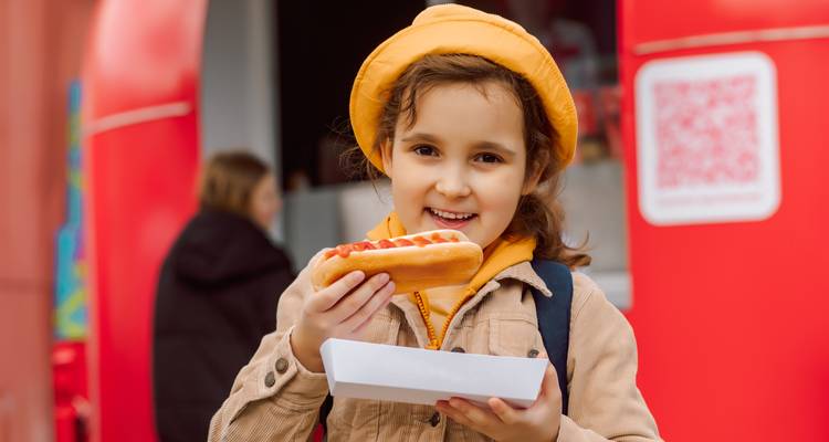 Un enfant tenant un hot-dog avec une expression joyeuse.