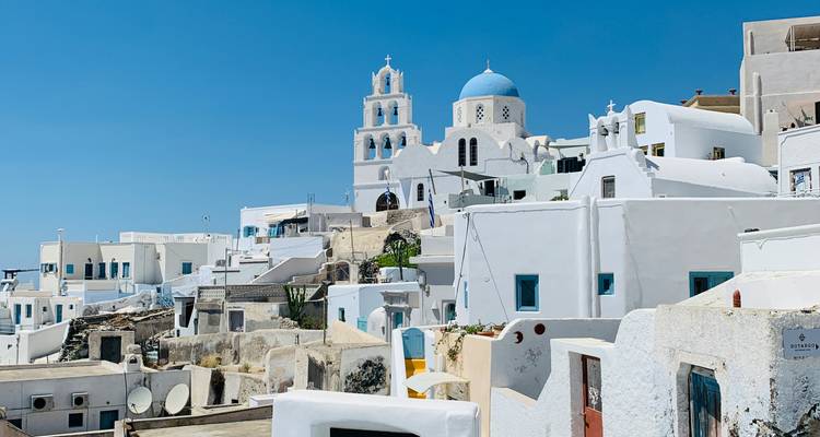 Bâtiments blancs avec une église au dôme bleu sous un ciel bleu dégagé.