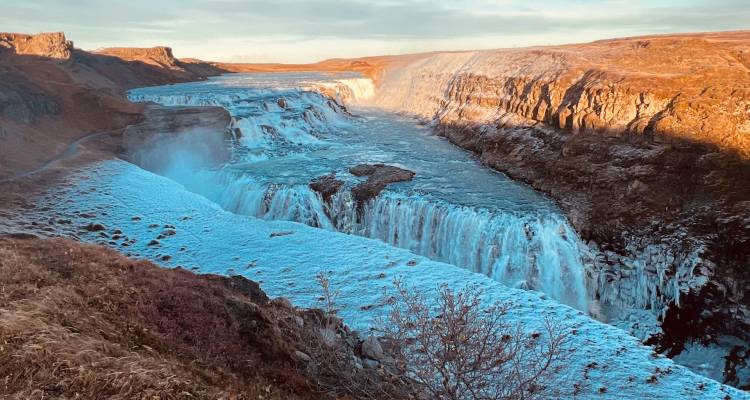Impressive waterfall in a canyon with snow and bare shrubs.