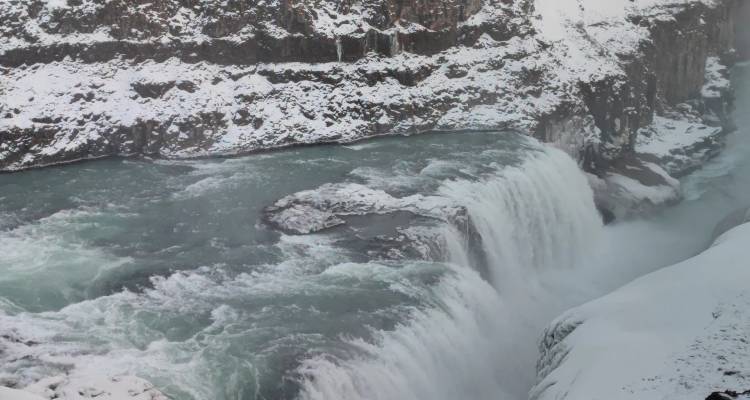 Powerful waterfall cascading into a river with snowy surroundings.