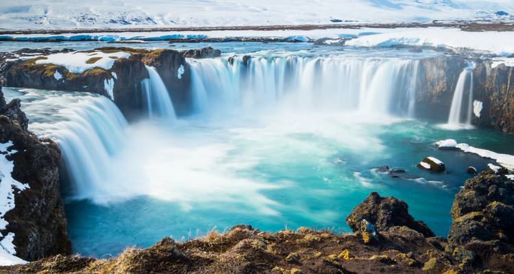 A wide waterfall with light mist and snowy surroundings.