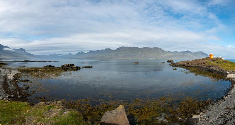 Paysage côtier avec montagnes et un phare.