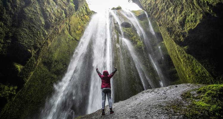 Personne sous une cascade avec les bras levés.